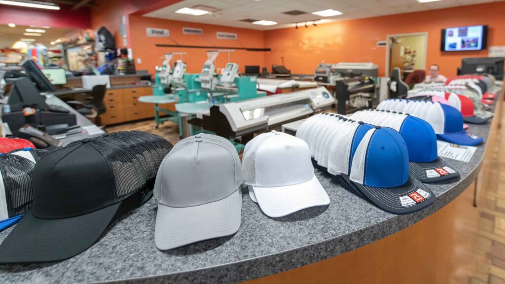 Variedad de gorras de camionero en blanco de diferentes colores expuestas en un mostrador dentro de una imprenta personalizada.