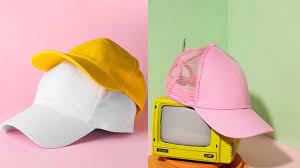 Una gorra blanca y otra amarilla a la izquierda, y una gorra de camionero rosa a la derecha, sobre fondos de colores pastel con atrezzo televisivo vintage.