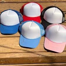 Una colección de cinco gorras de camionero en rojo, azul, rosa, negro y azul claro, todas ellas con paneles frontales blancos y parte trasera de malla, dispuestas sobre una superficie de madera.