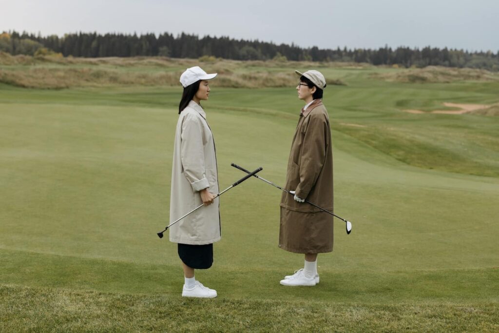 Två golfare i långa rockar och kepsar står ansikte mot ansikte på en grön golfbana och håller klubborna korsade mellan sig.