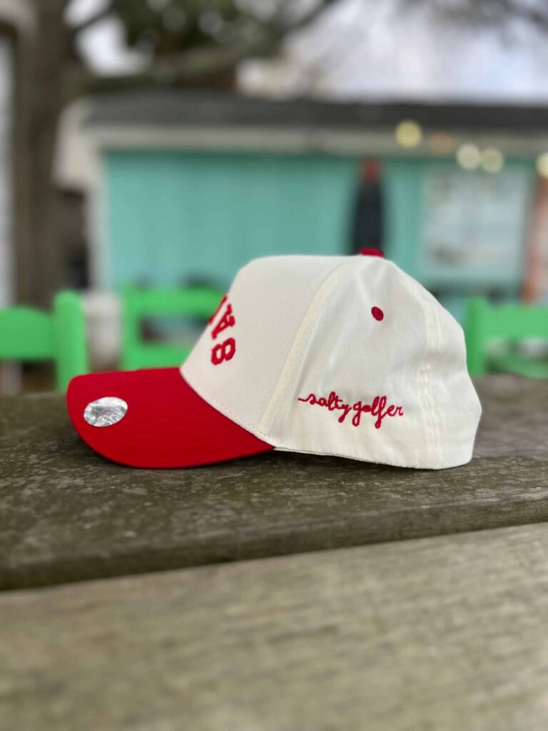 White and red golf cap with salty golfer embroidery on wooden table