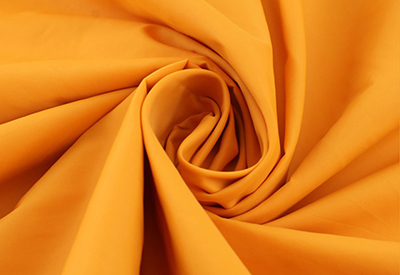 Close-up of smooth orange fabric folded in a swirl pattern.