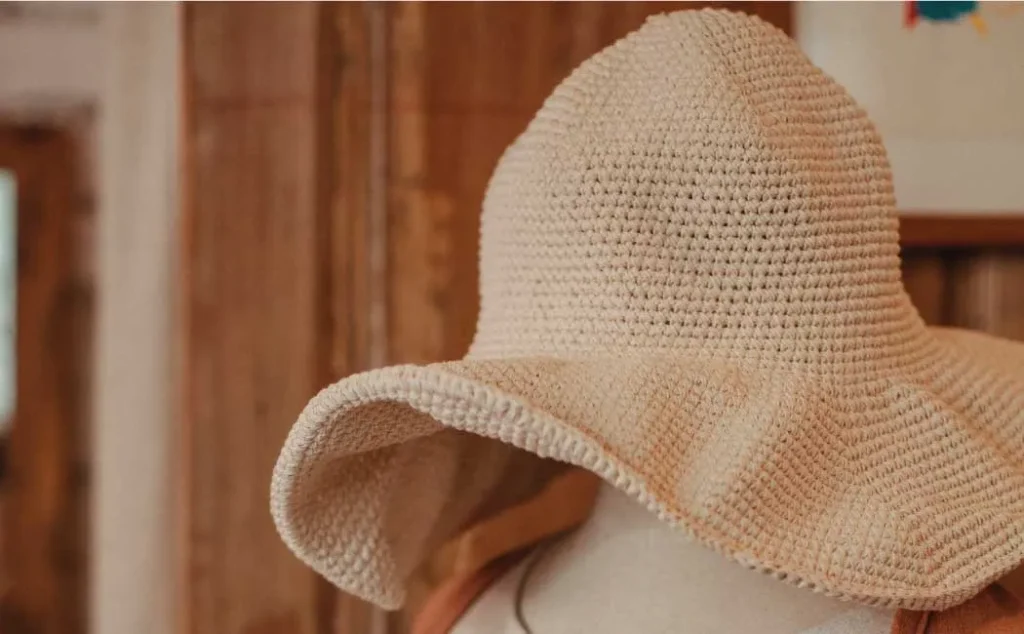 Close-up of beige crochet sun hat with wide brim on mannequin indoors.