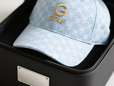 Light blue golf cap with gold embroidered "G GOLF" logo inside black presentation box.