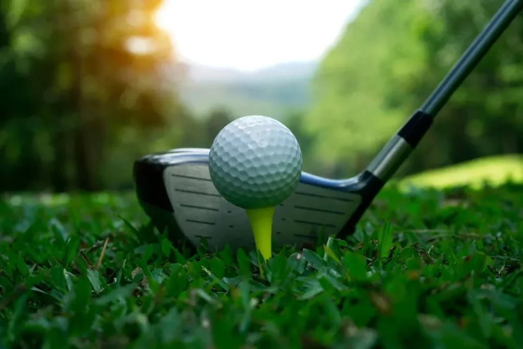 Close-up of a golf ball on a yellow tee with a driver club poised to strike, surrounded by lush green grass.