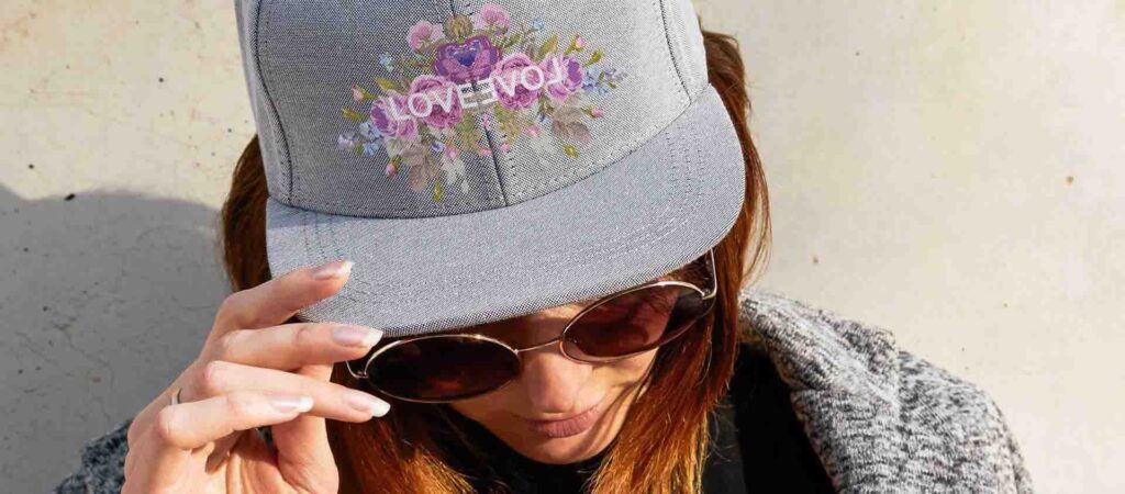 Woman wearing a grey cap with floral embroidery and "LOVE YOU" text design.
