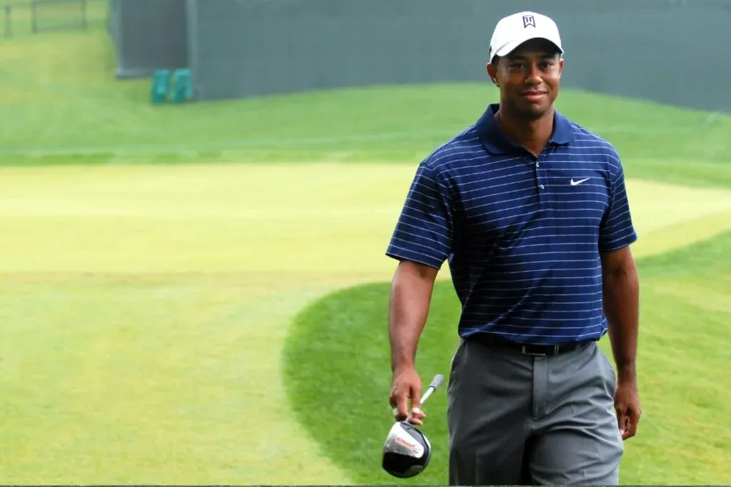 Smiling golfer in a striped polo and white cap walking on the fairway holding a driver club.