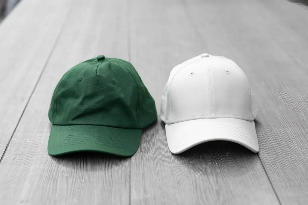 Green and white baseball caps placed side by side on a wooden floor