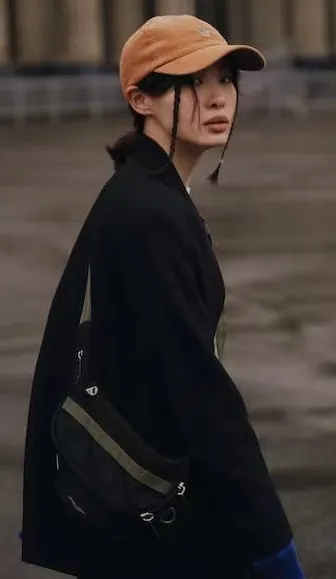 Woman with black coat and brown baseball cap looking over shoulder outdoors.