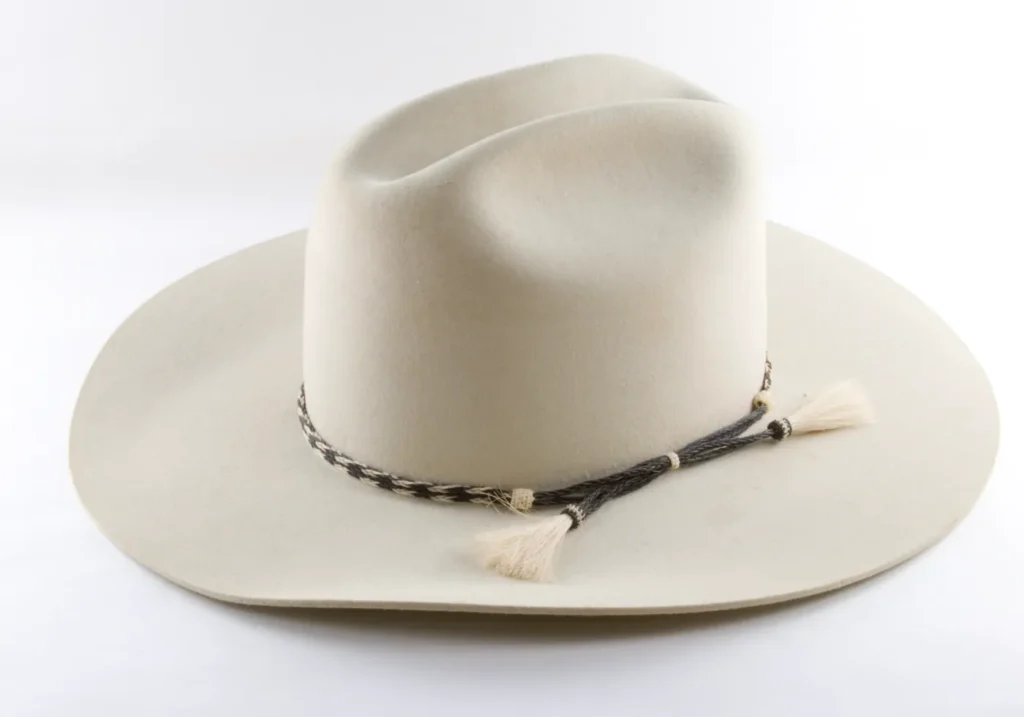 Beige felt hat with black and white braided band and tassels on white background.