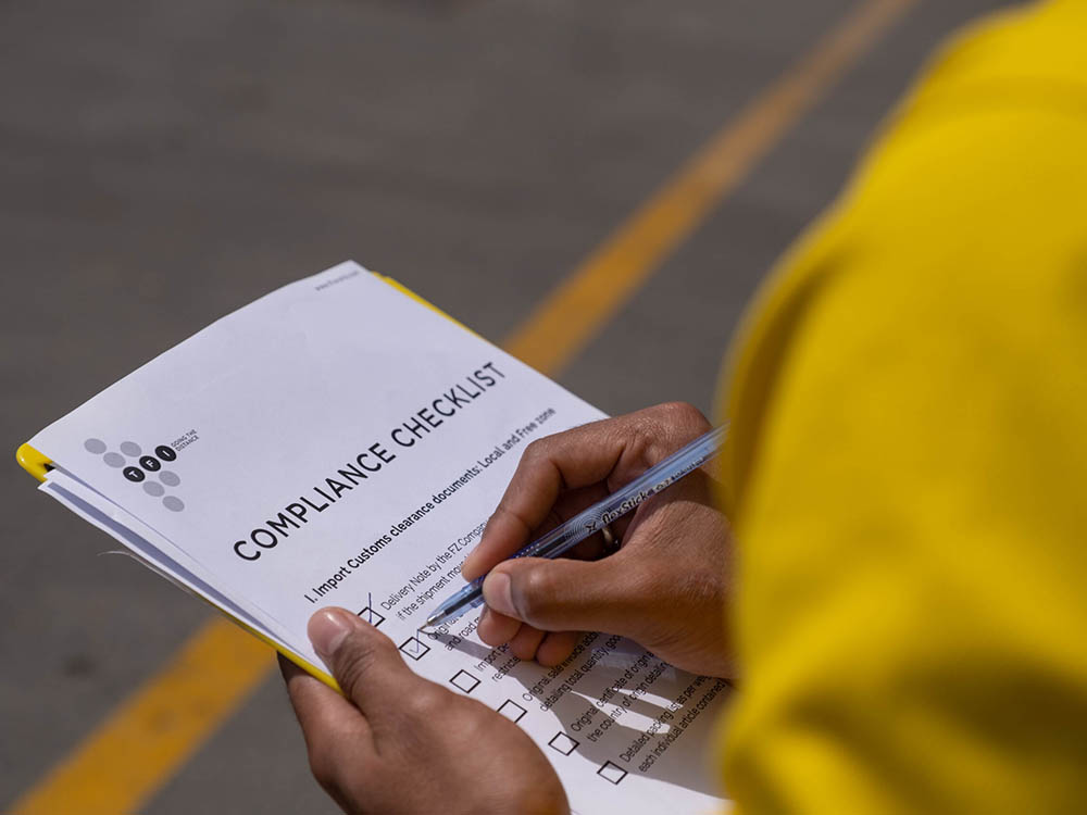 Person marking boxes on a printed compliance checklist with a pen outdoors.