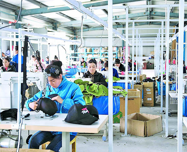 Workers sewing and assembling hats in busy factory with materials and boxes around.