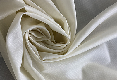 Close-up of cream-colored ripstop fabric with grid pattern and folds.