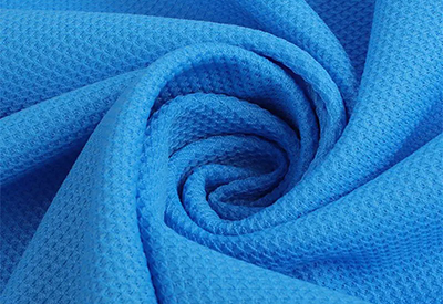 Close-up of blue waffle weave fabric with textured surface and swirling folds.
