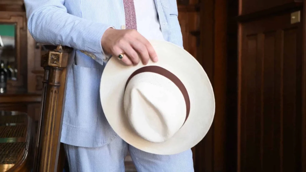 Man in striped suit holding Panama fedora indoors.