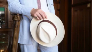 Man in striped suit holding Panama fedora indoors.