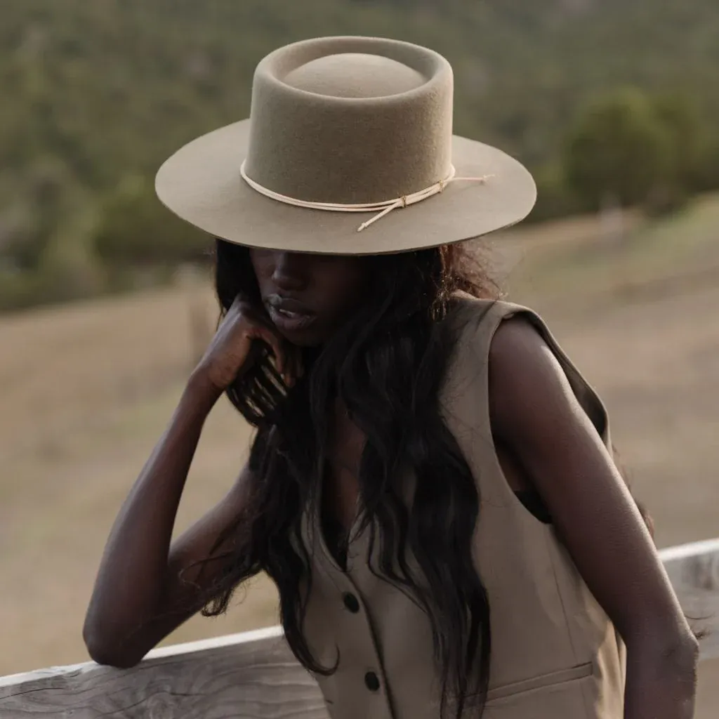 Woman wearing a beige wide brim hat and matching vest, leaning on wooden railing outdoors