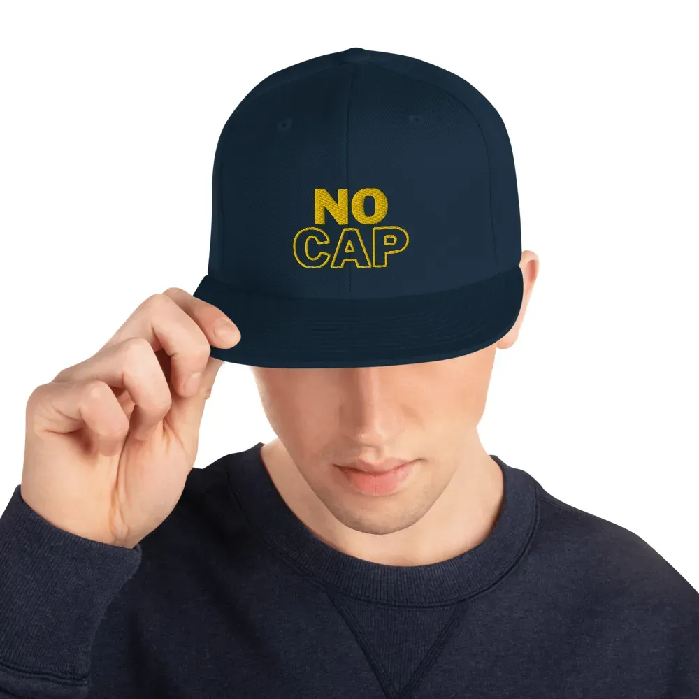 Man wearing navy snapback cap with "NO CAP" embroidery.