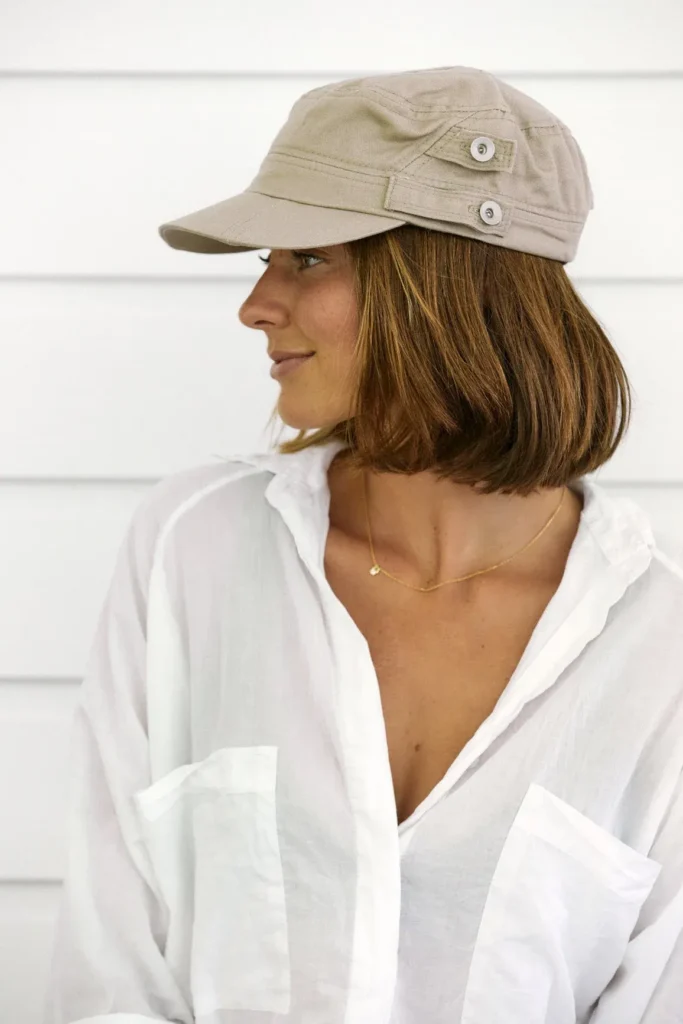 Woman wearing beige cotton army-style cap and white shirt, looking sideways.