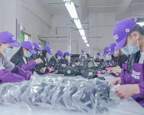 Workers inspecting caps in factory wearing purple uniforms and masks.