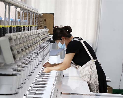 Woman operating embroidery machine in factory.