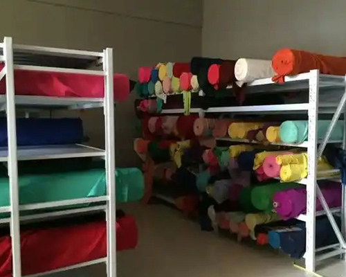 Rolls of colorful fabric stored on shelves in warehouse.