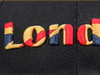 Colorful embroidered "London" text with red, blue, and yellow thread on black fabric.