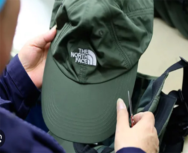 Person examining green The North Face cap with needle in hand.