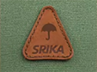 Brown triangular leather patch with umbrella icon and "SRIKA" text on green fabric.