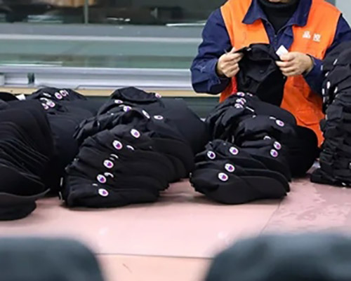 Worker inspecting stacks of black caps on table.