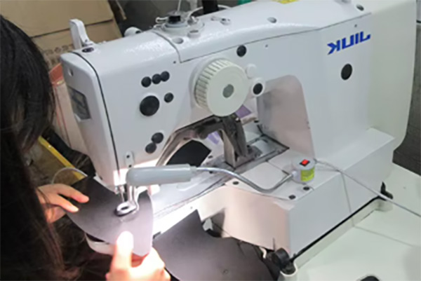 Person stitching black fabric using industrial sewing machine in workshop.