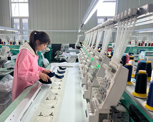 Worker operating embroidery machine on caps in factory.
