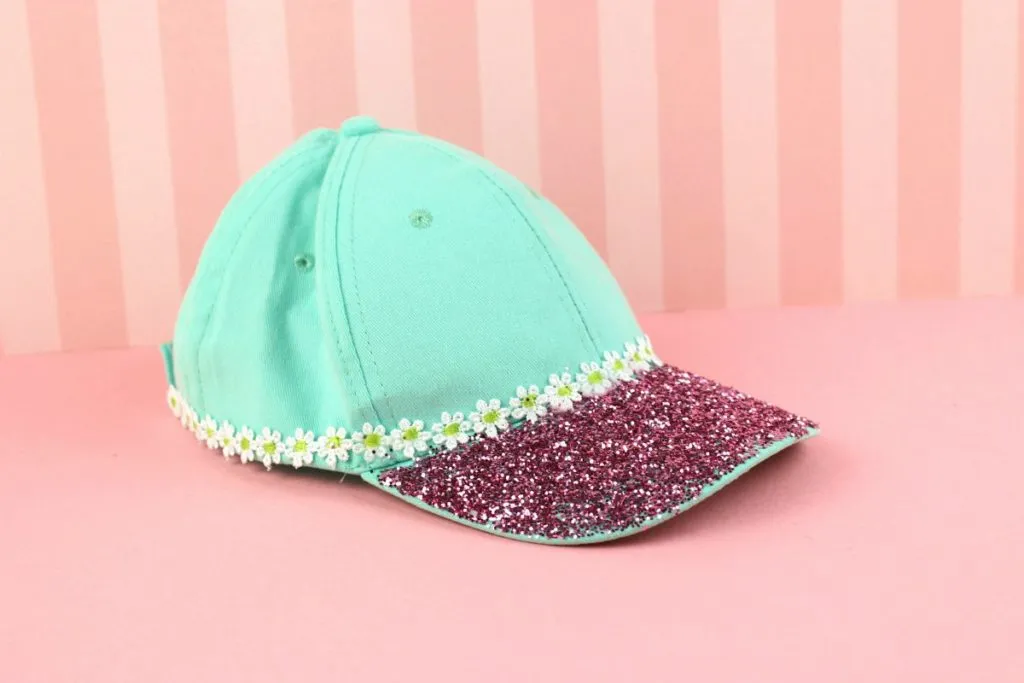 Mint green cap with glittery pink brim and floral trim on pink background.