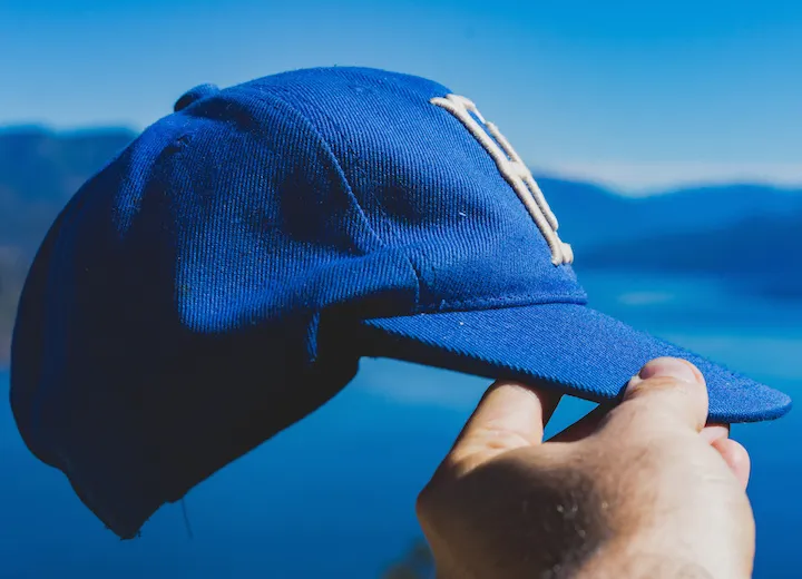 Hand holding blue baseball cap with mountain background
