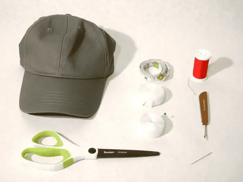 Baseball cap with sewing tools including scissors, thread, measuring tape, and needles.
