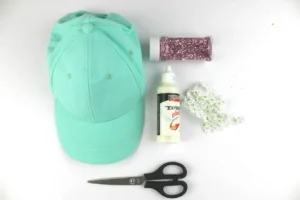 Mint cap with glitter, glue, scissors, and flower trim for decoration.
