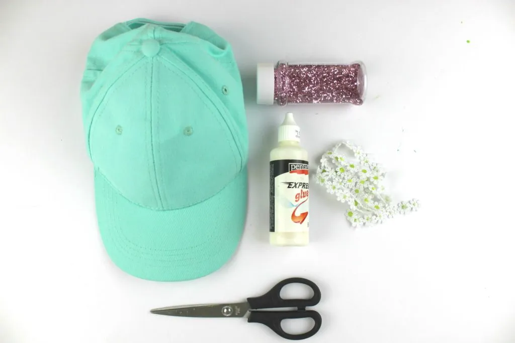 Mint cap with glitter, glue, scissors, and flower trim for decoration.