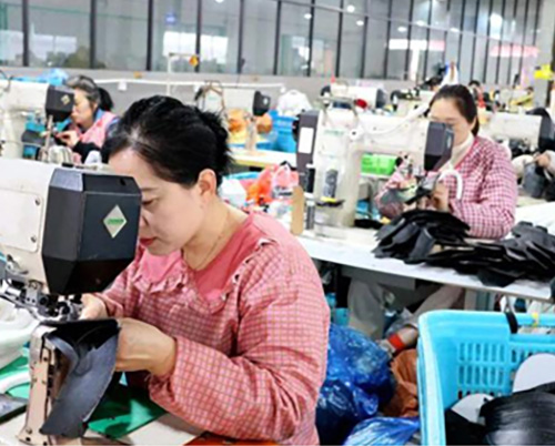 Women sewing with machines in busy garment factory.