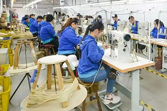 Workers sewing hats on machines in a factory setting.