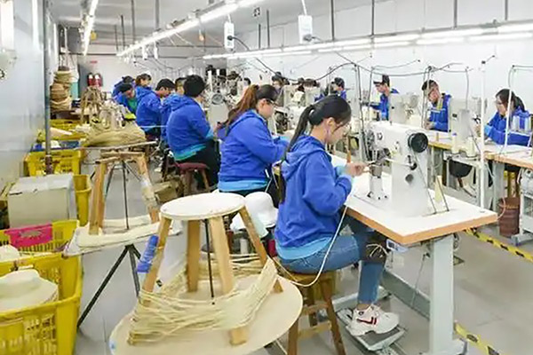 Workers sewing hats on machines in a factory setting.