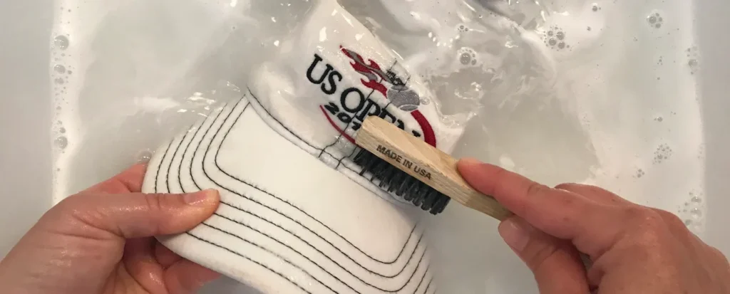 Hand scrubbing white cap with brush in soapy water