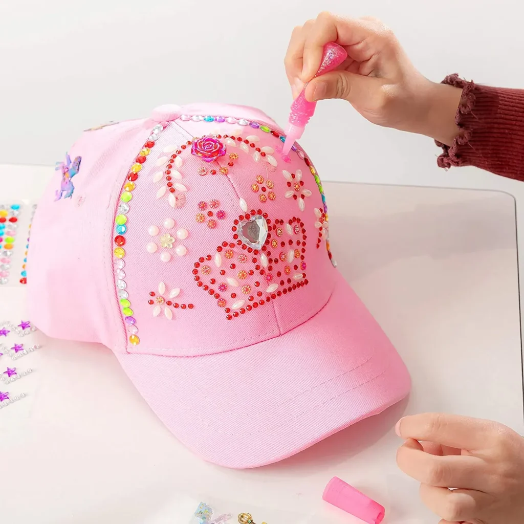 Hands decorating pink cap with rhinestones and glue for design.