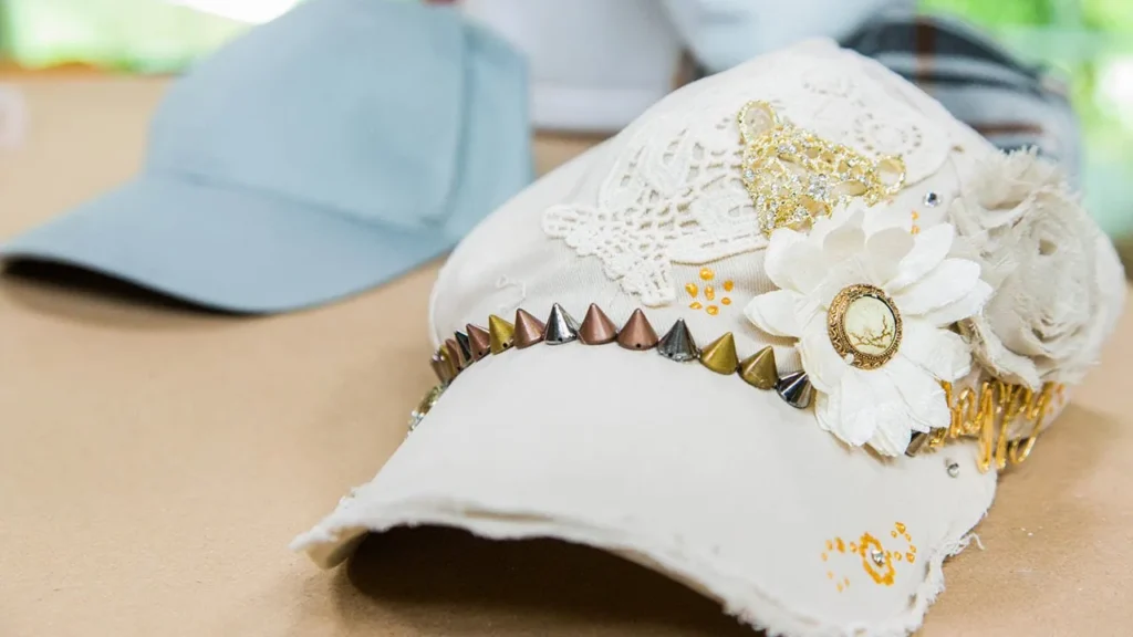 Beige cap decorated with fabric flowers, studs, and lace details.