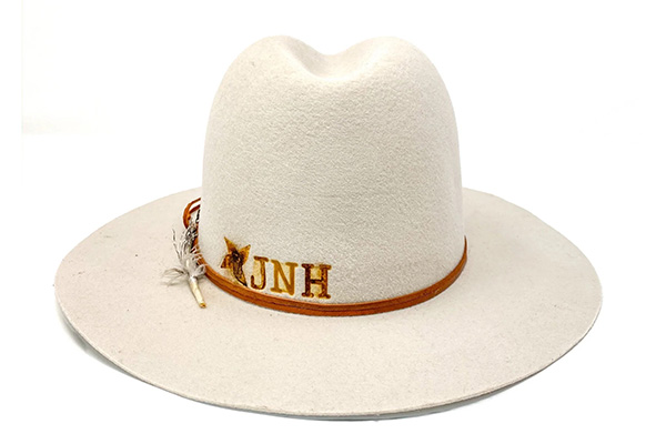White felt cowboy hat with brown leather band and decorative feather.