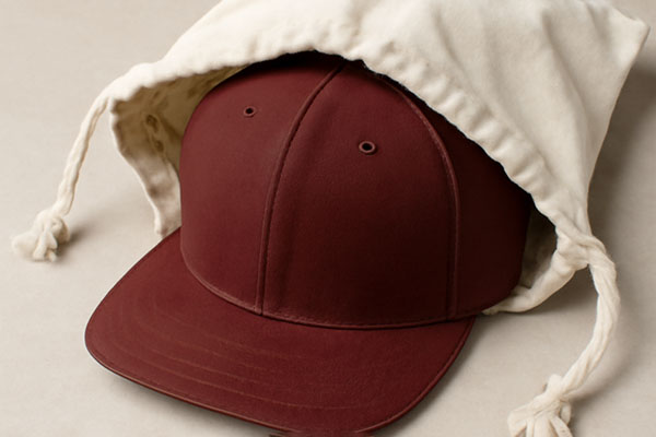 Burgundy baseball cap partially inside a cream drawstring pouch.