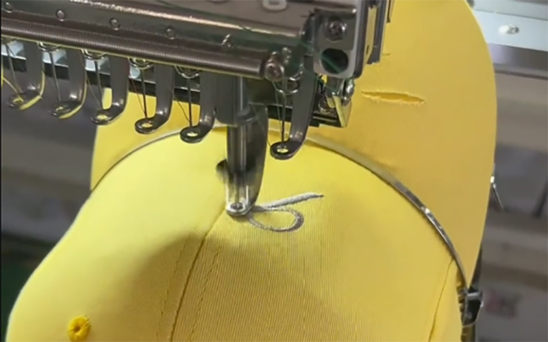 Close-up of a yellow cap being embroidered with a logo design on a machine.