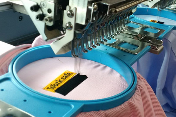 Automatic embroidery machine stitching "Work Safe" label on fabric.
