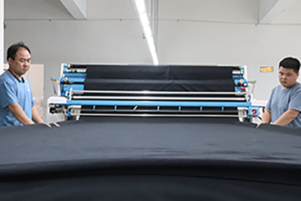 Two workers operating machine rolling out large black fabric sheets.