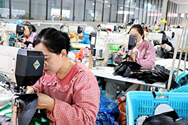 Women sewing fabric pieces at machines in busy factory.
