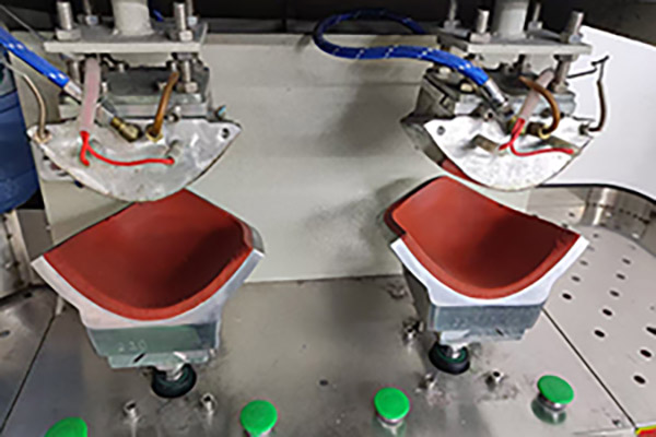 Industrial machine pressing red hat brims for shaping.